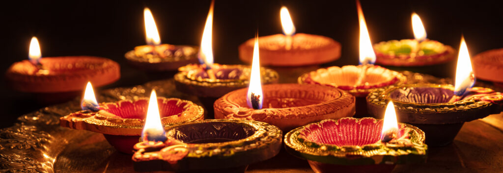 Happy Diwali. Clay diya candles illuminated in Dipavali, Hindu festival of lights. Traditional oil lamps on dark background, banner, closeup view